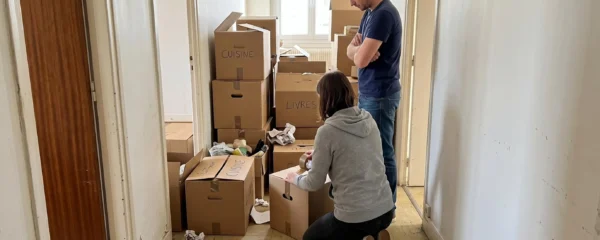 Couple entouré de cartons de déménagement dans un couloir d'appartement lumineux, s'apprêtant à organiser leur stockage