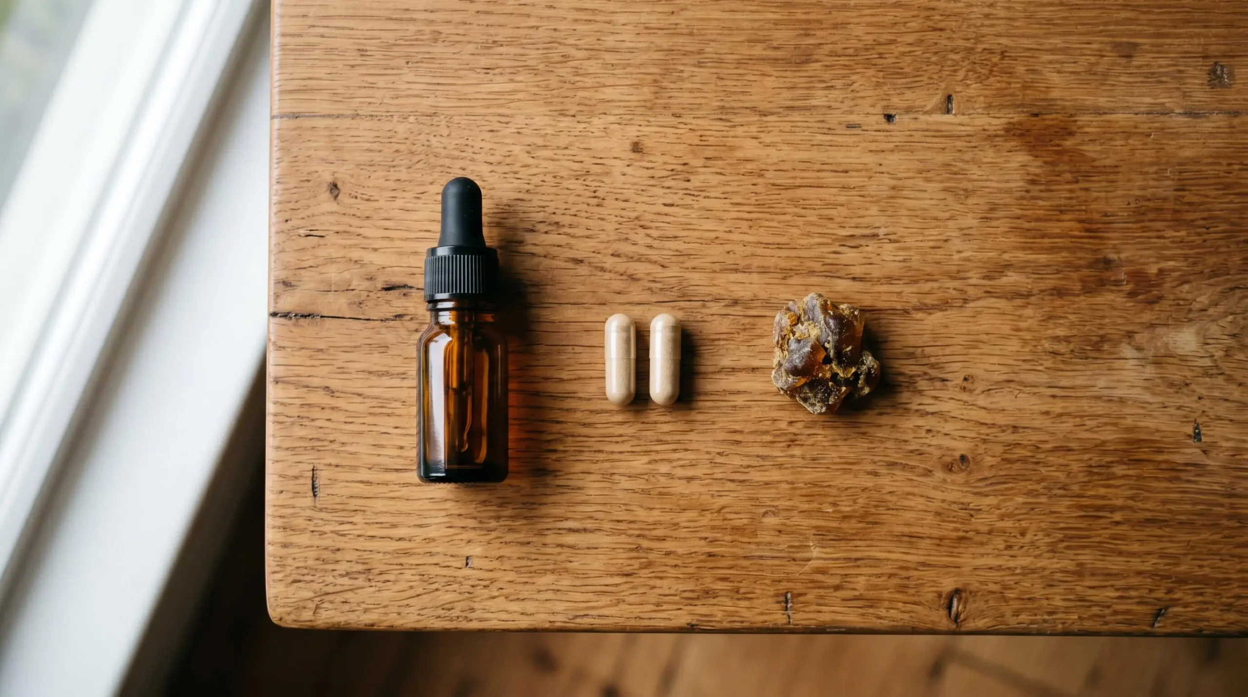 Présentation de différentes formes de produits CBD — huile, gélules et résine — posées sur une table en bois naturel