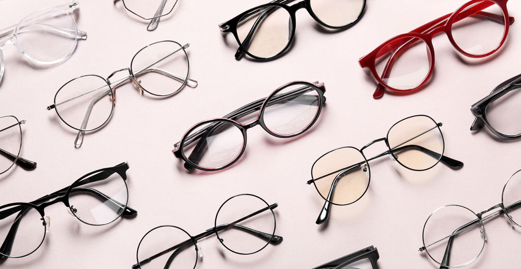 Trois montures de lunettes de vue alignées sur bois clair : acétate écaille havane brillant, métal doré rosé mat fin, titane gris anthracite brossé, gros plan révélant textures contrastées
