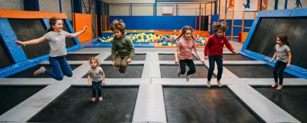 Groupe d'enfants sautant activement sur des trampolines dans un parc de loisirs indoor lors d'une fête d'anniversaire