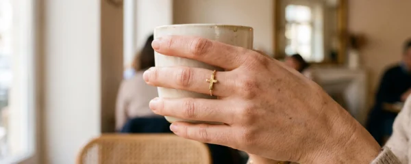 Gros plan d'une main de femme portant une bague croix en plaqué or tenant une tasse dans un café