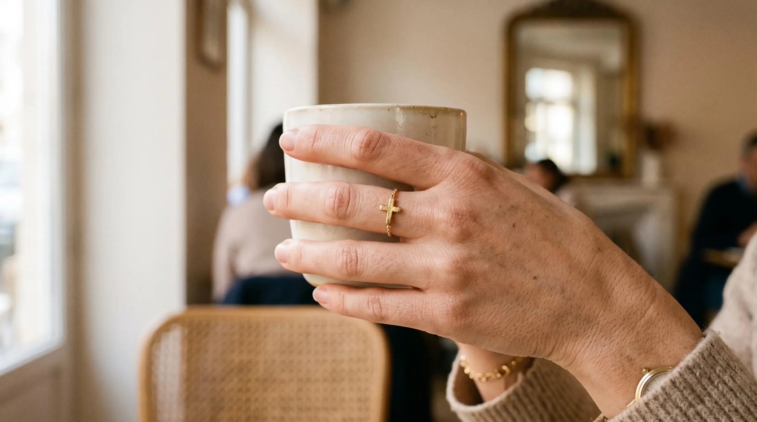 Gros plan d'une main de femme portant une bague croix en plaqué or tenant une tasse dans un café