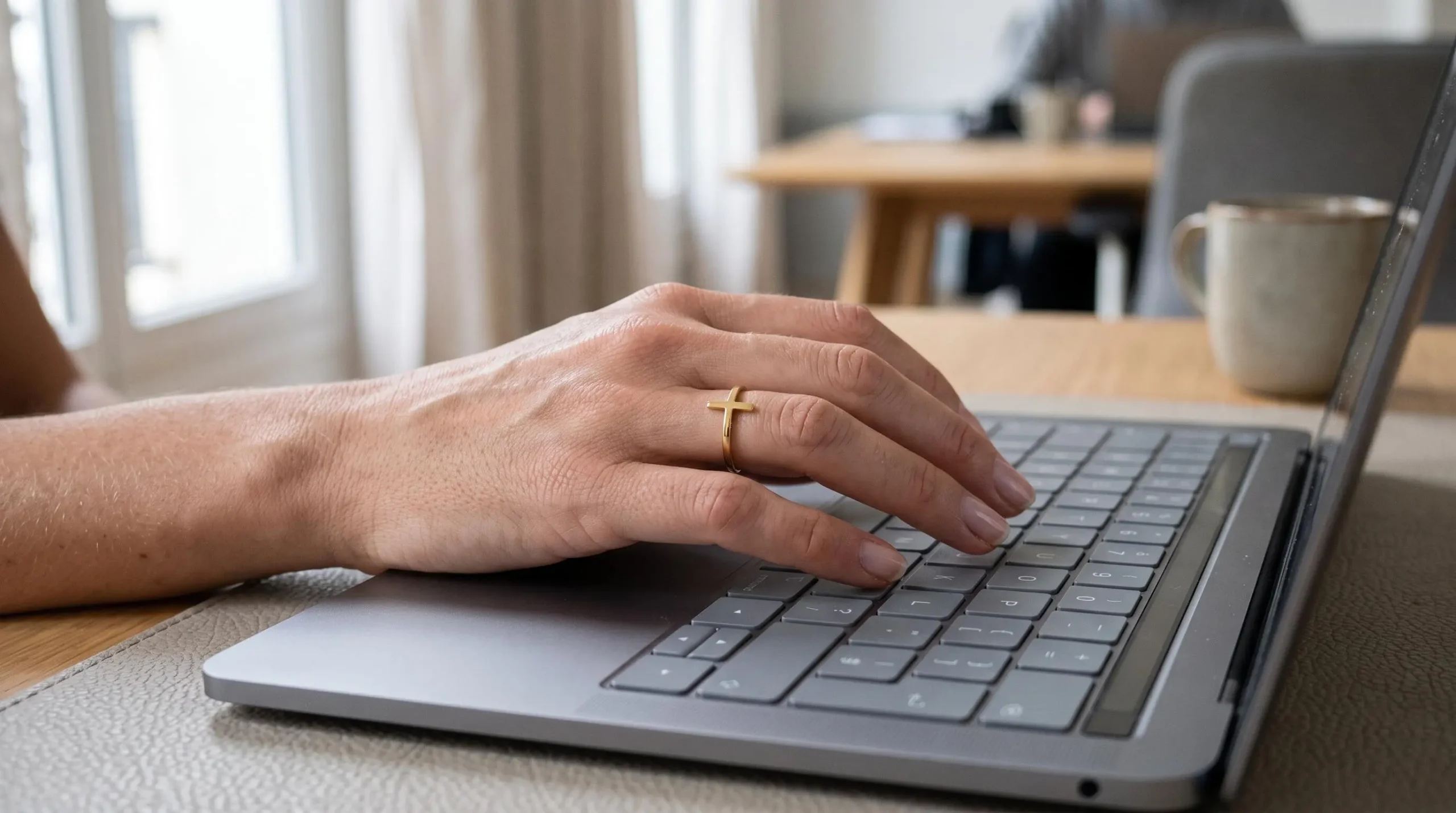 Main de femme portant une bague croix en plaqué or en train de taper sur un clavier d'ordinateur au bureau